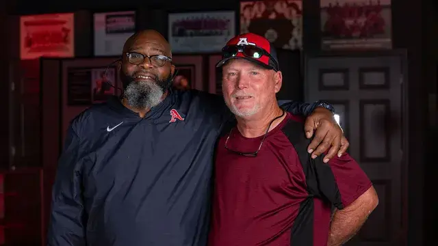 Two men with arms around each other's shoulders, one in a Devils cap.