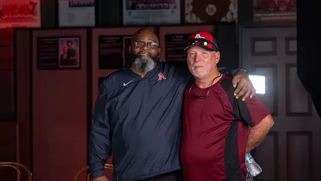 The same two men, one in a Devils cap, smile for the camera.