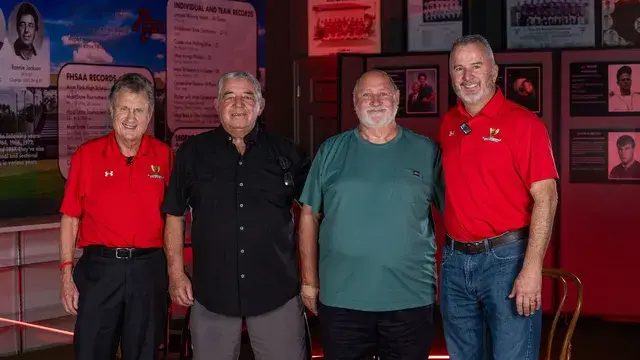 Four men pose in front of the records display.