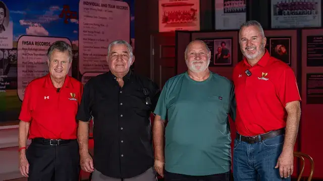 The same four men, arms at their sides, in front of the records display.