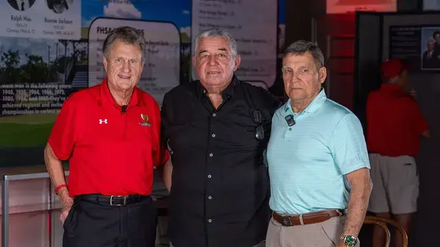 Three men pose in front of the records display.