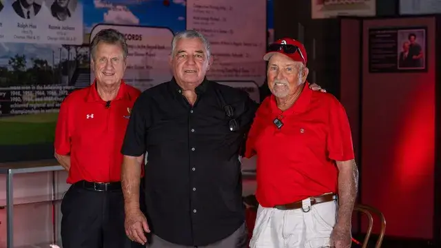 Three men, two in red polos and one in black, pose in the gallery.