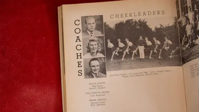 A yearbook page of coaches and cheerleaders laid on red cloth.