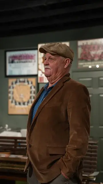 A man in a flat cap and corduroy jacket stands in the gallery.