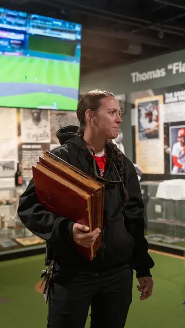 A woman carrying a wooden case walks through the gallery beneath a screen.