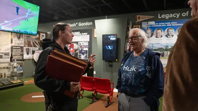 The woman with the case and a visitor in a Huk shirt talk in the gallery.