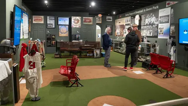 The gallery: stadium seats, vintage uniforms on stands, and visitors on the turf.