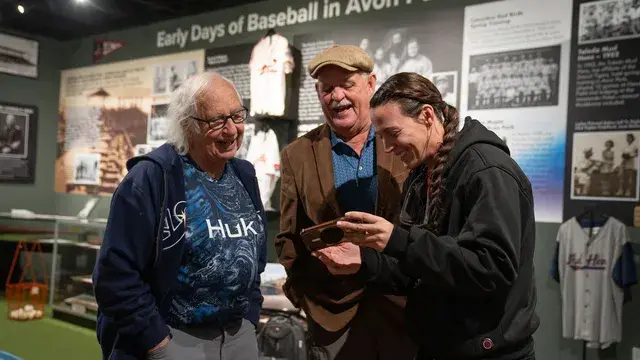 Three people laugh over a phone in front of the Early Days panel.