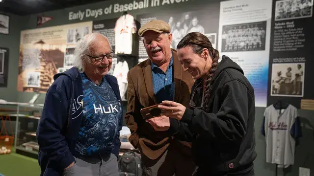 Three visitors look at a phone together in the gallery.